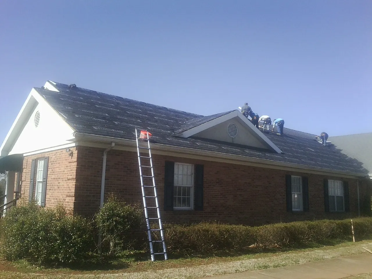 Crew tearing shingles off a brick ranch roof with a ladder set — Metal Roof Repair work by our crew in Bloomington